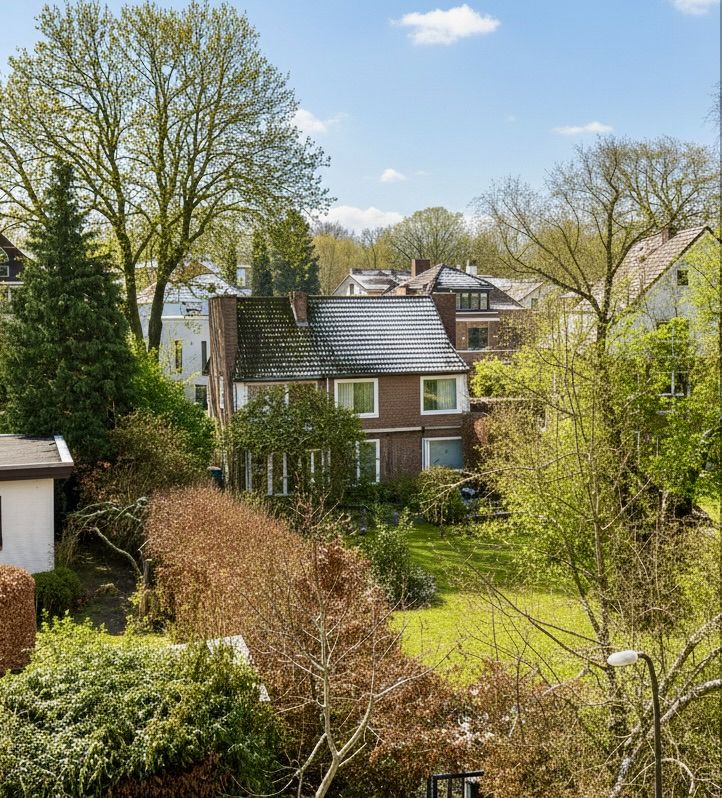 Zweistöckiges Backsteinhaus mit großem Garten und vielen Bäumen, umgeben von weiteren Häusern.