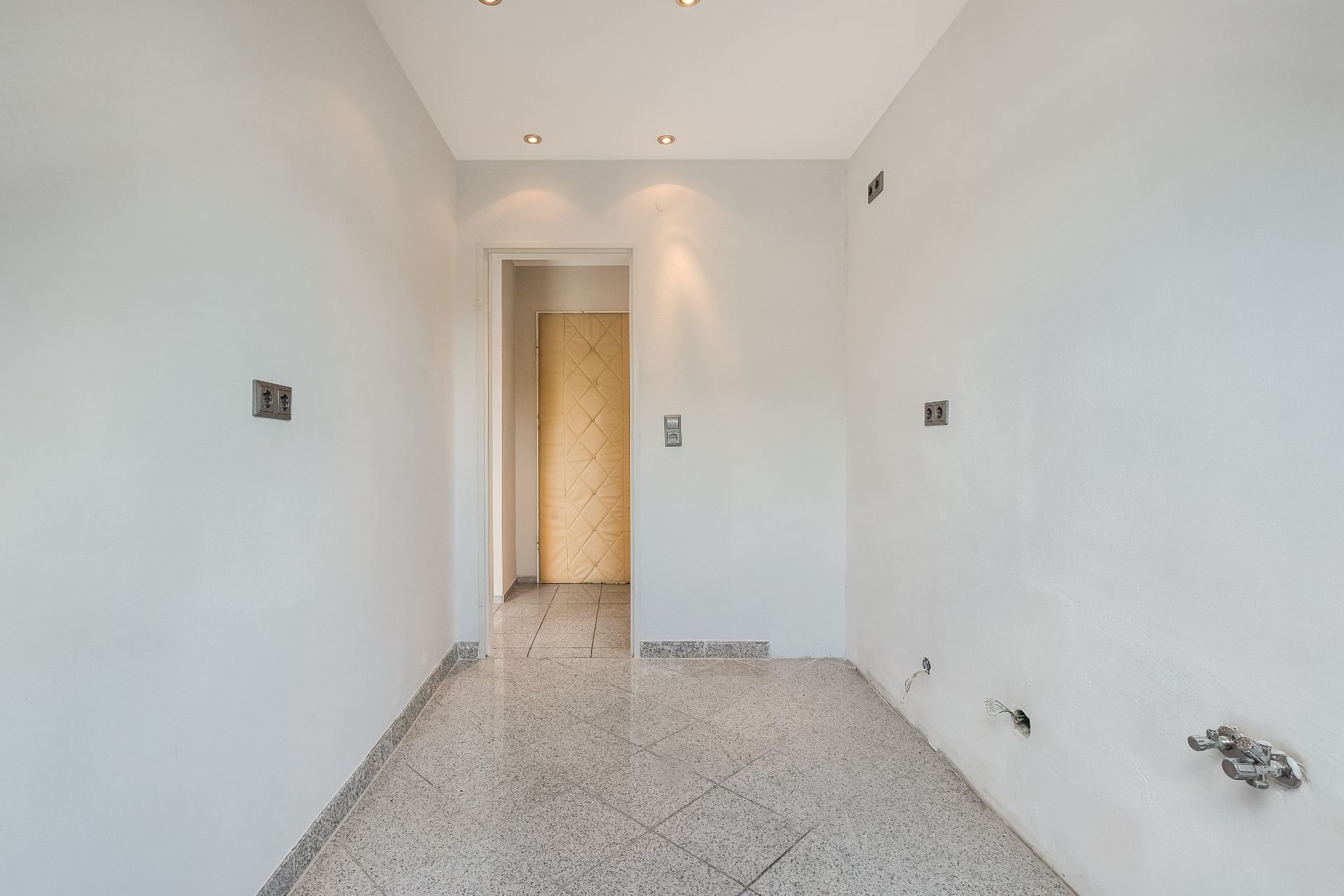 Leerer Raum mit hellen Wänden, Fliesenboden und mehreren Steckdosen an den Wänden.