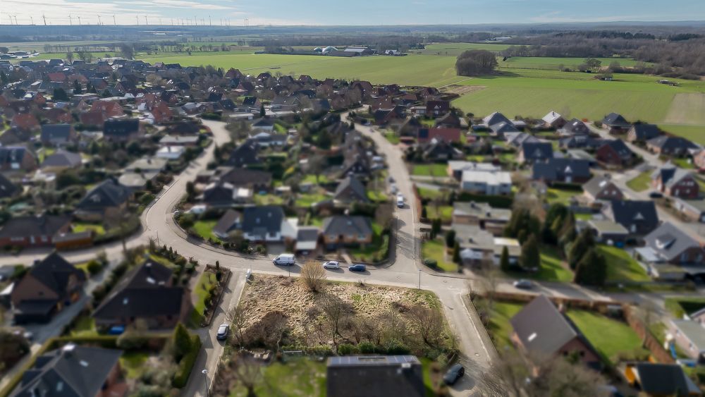 Luftaufnahme eines Wohngebiets mit Einfamilienhäusern und einem leeren Grundstück in der Mitte.