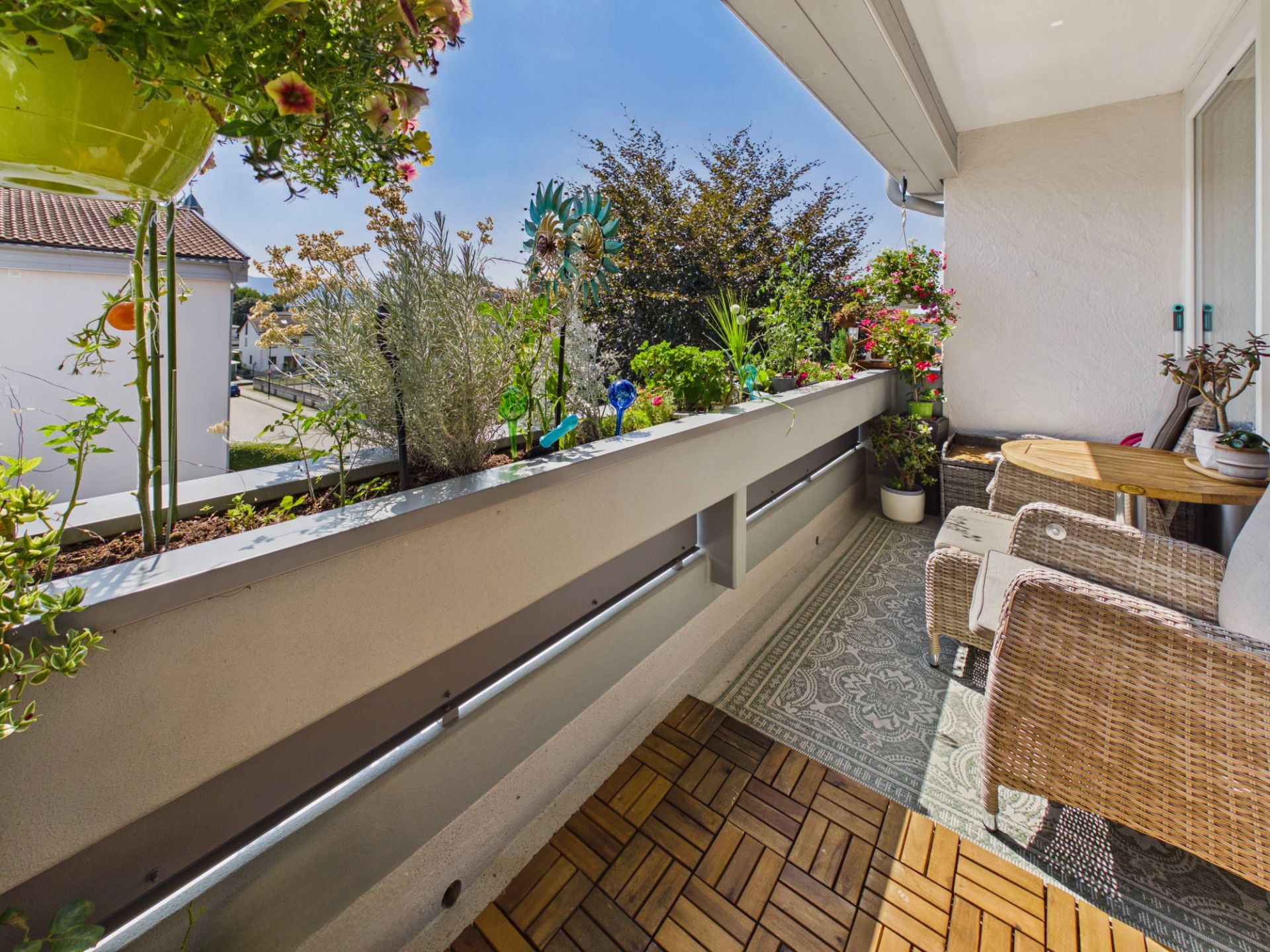Balkon mit Korbstühlen, Holztisch und vielen Pflanzen auf der Brüstung.