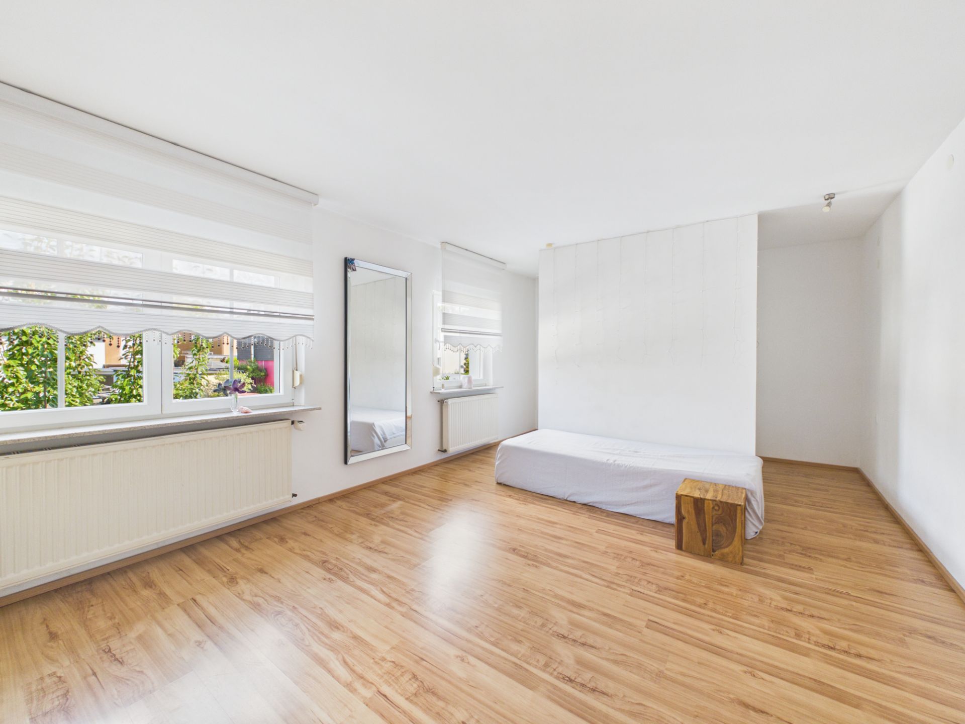 Helles Schlafzimmer mit Holzboden, einem Bett, einem Spiegel und großem Fenster.