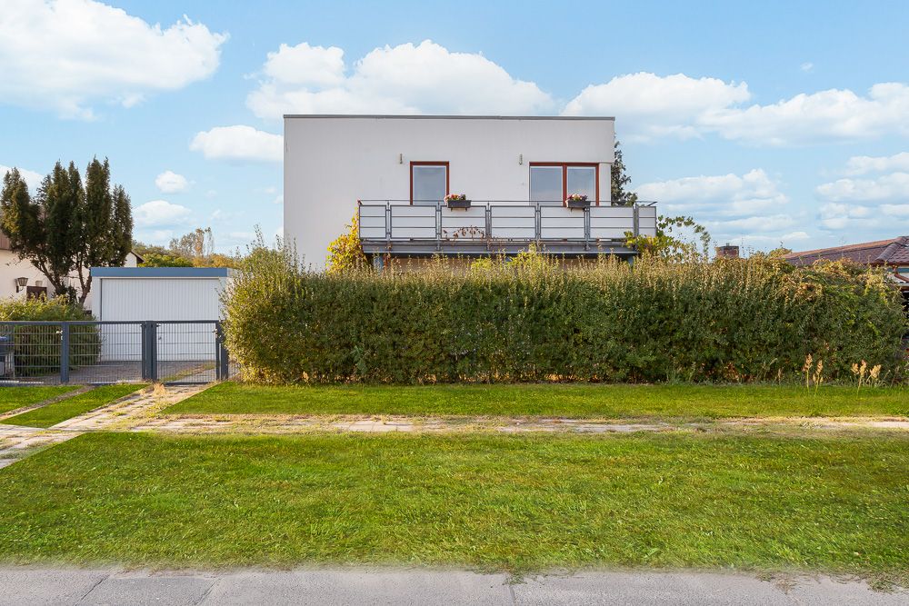 Modernes Wohnhaus mit großem Balkon und hoher Hecke im Vorgarten.