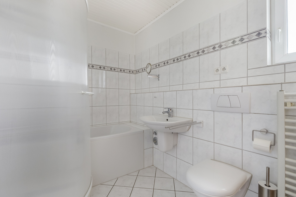Helles Badezimmer mit Badewanne, Waschbecken, WC und weiß gefliesten Wänden.