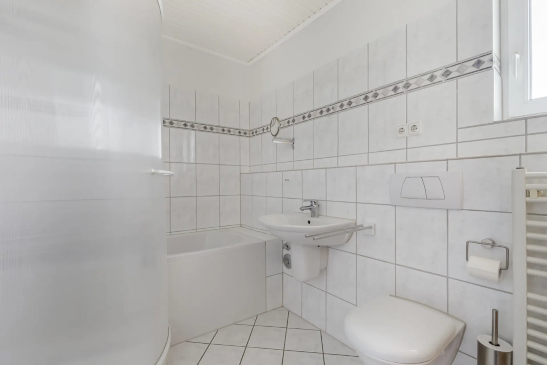 Helles Badezimmer mit Badewanne, Waschbecken, WC und weiß gefliesten Wänden.