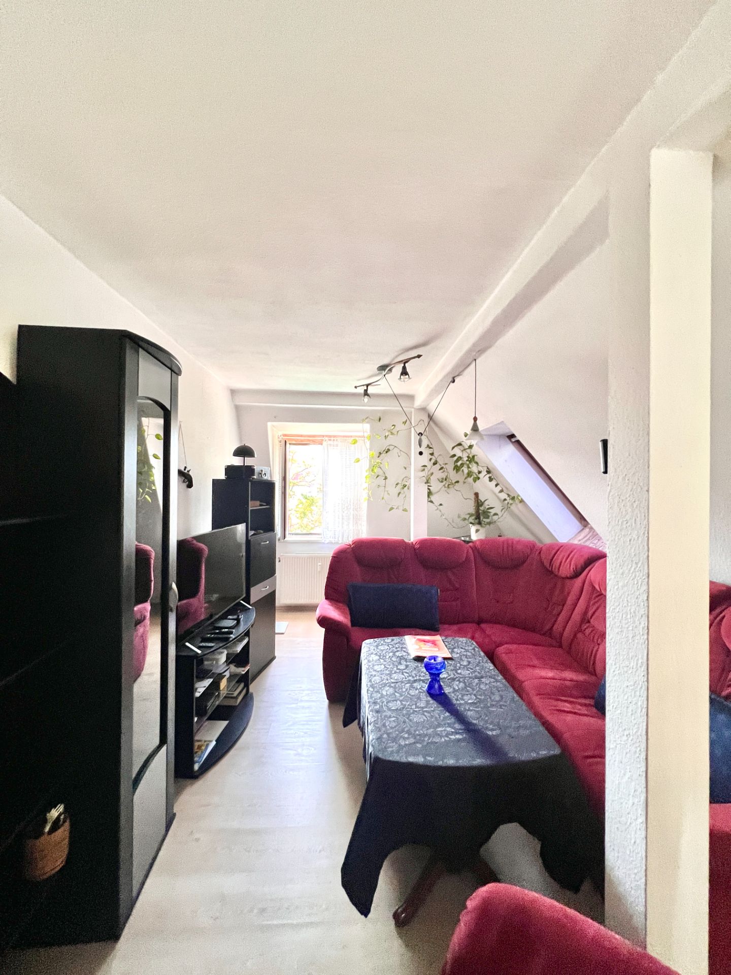 Wohnzimmer mit rotem Ecksofa, Couchtisch, schwarzem Schrank und Fernseher, Fenster im Hintergrund.