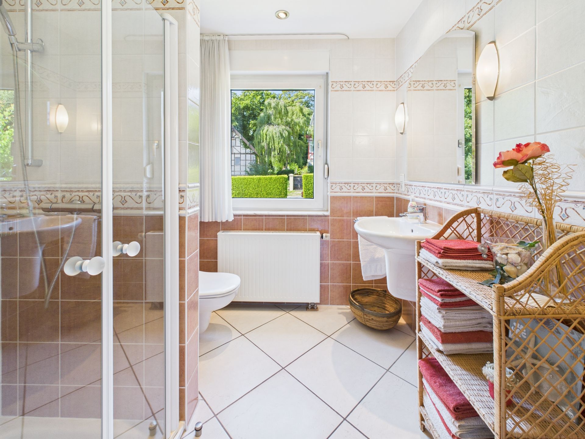 Helles Badezimmer mit Dusche, Waschbecken, Fenster und Regal mit Handtüchern.