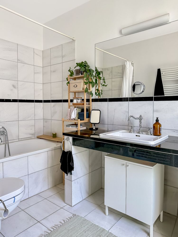 Modernes Badezimmer mit Badewanne, Waschbecken, Spiegel und Regal mit Pflanze.