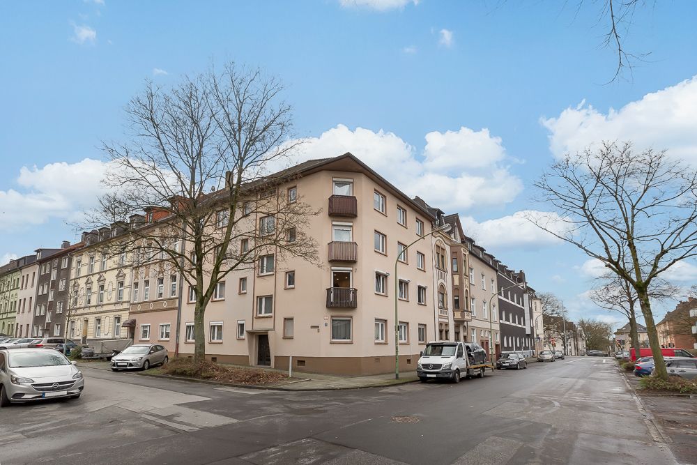 Eckwohnhaus mit mehreren Etagen, Balkonen und geparkten Autos an einer Kreuzung.