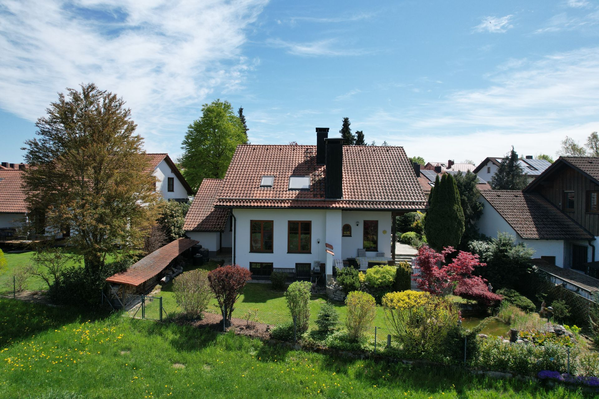 Einfamilienhaus mit rotem Dach, Garten und Bäumen an einem sonnigen Tag.