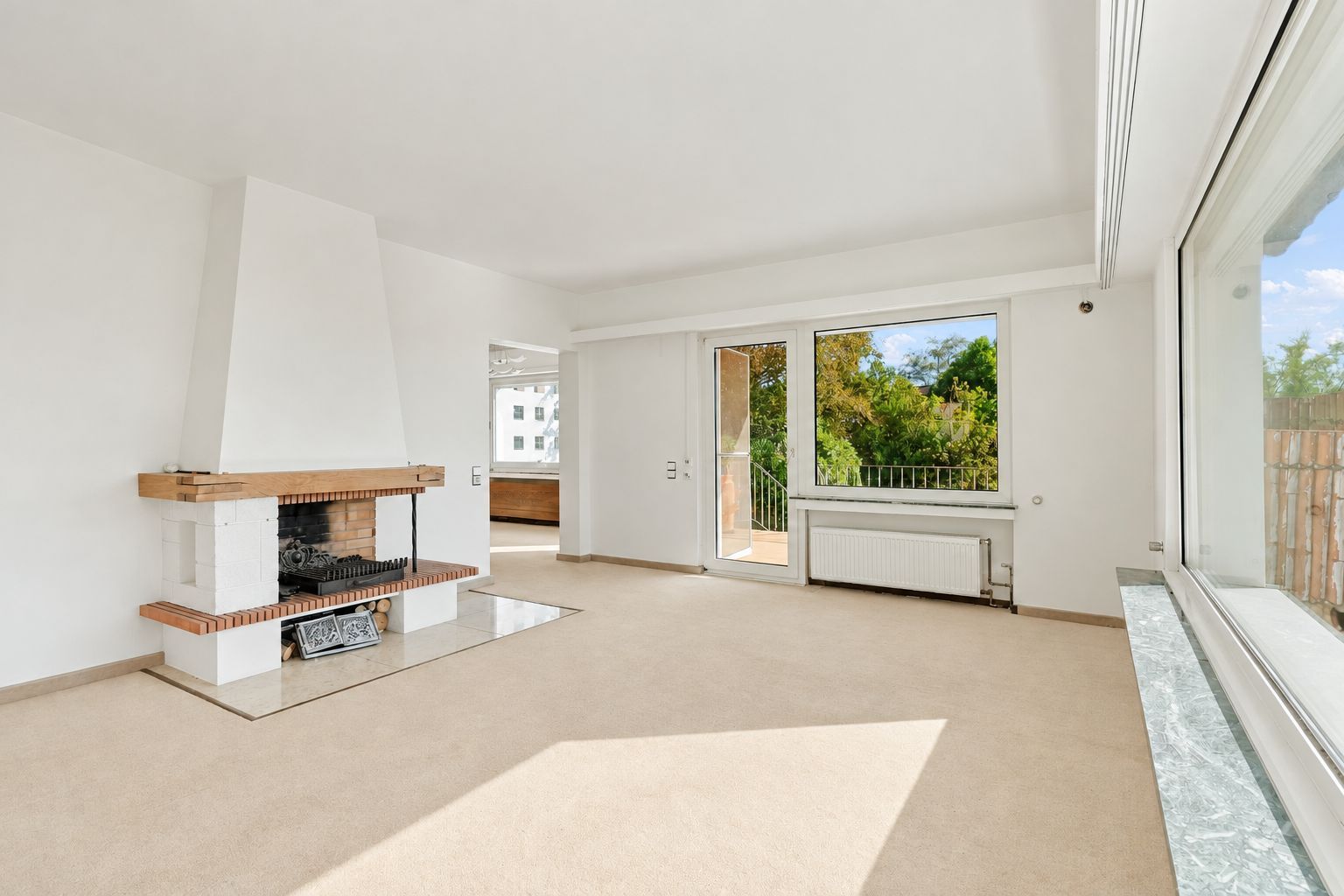 Helles Wohnzimmer mit Kamin, großen Fenstern und Zugang zu einem Balkon.