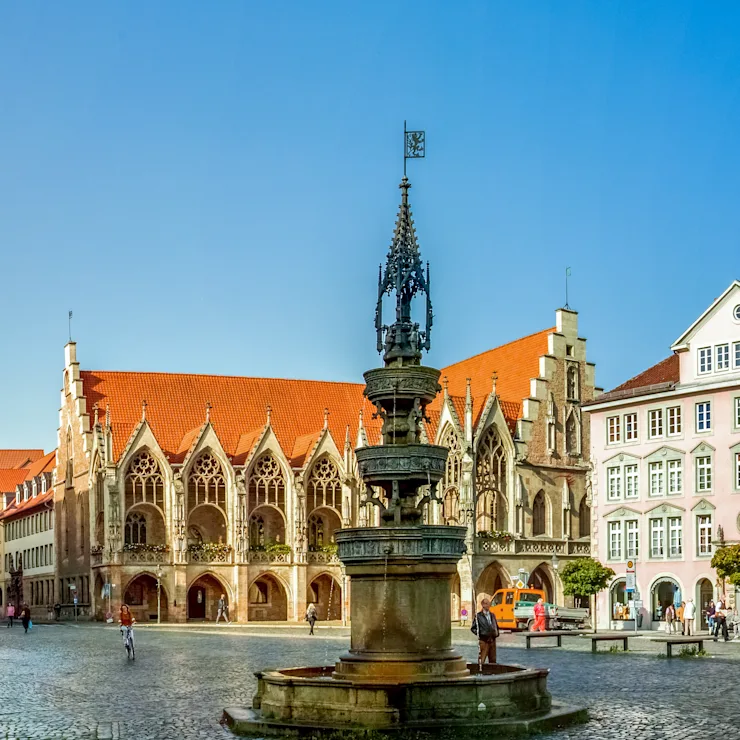 Historischer Platz mit Brunnen, Kirche und umliegenden Gebäuden bei klarem Himmel.