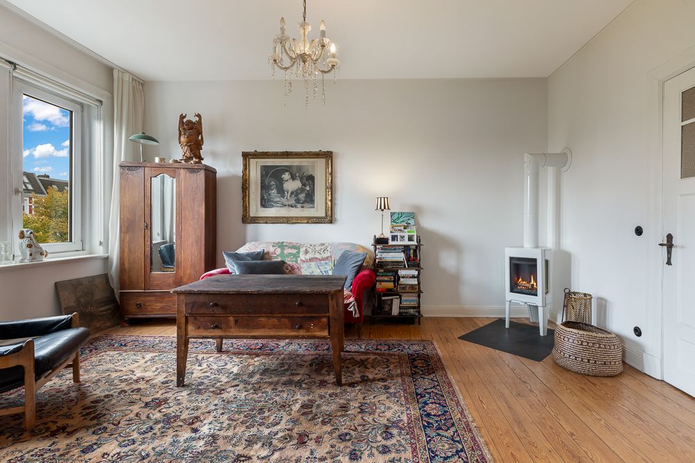 Gemütliches Wohnzimmer mit Teppich, Sofa, Holzschrank, Kaminofen und großem Fenster.