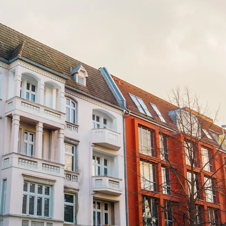 Mehrstöckige Wohnhäuser mit Balkonen und großen Fenstern, ein Baum im Vordergrund.