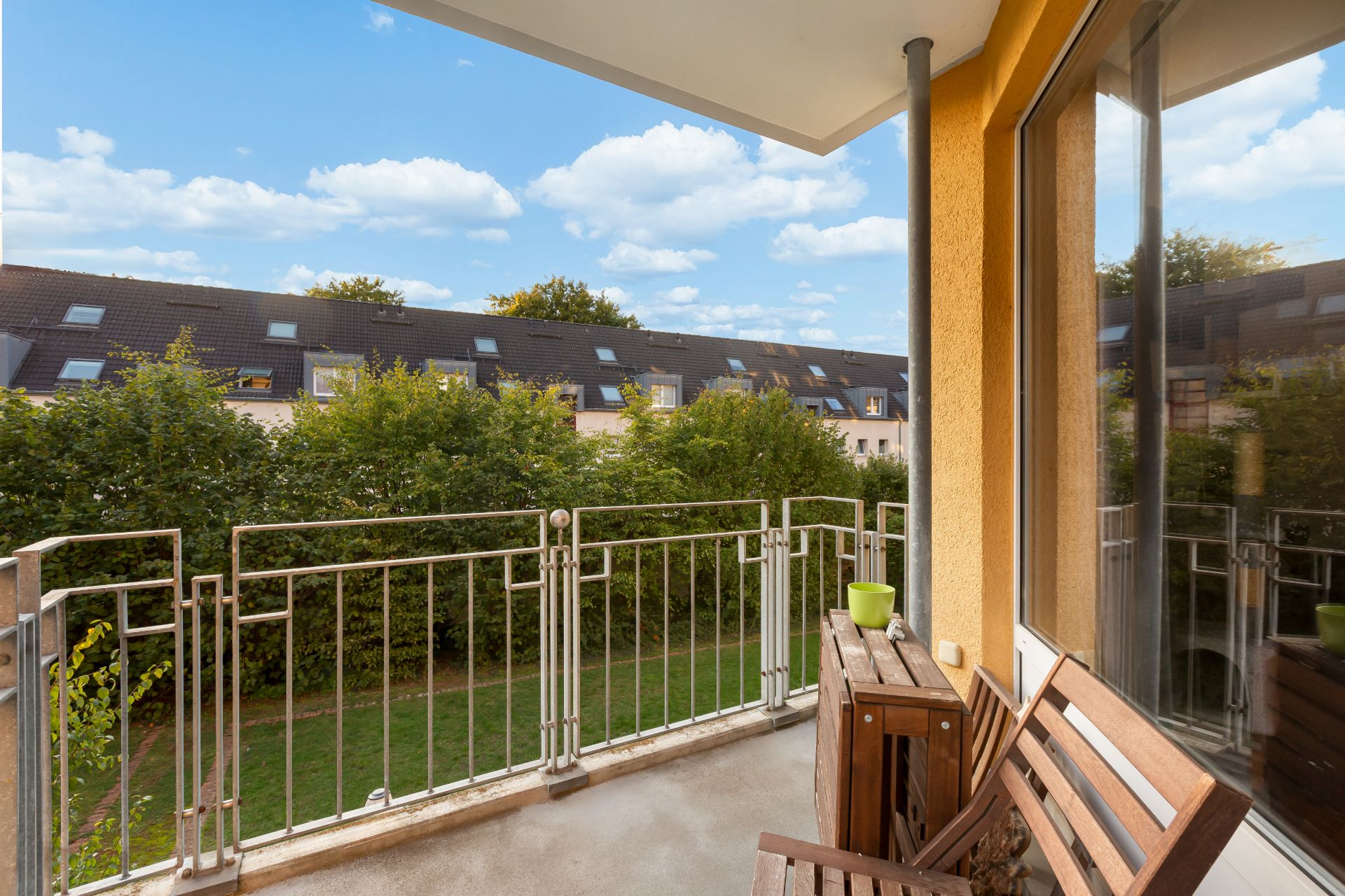 Balkon mit Holzmöbeln und Blick auf Garten und Nachbarhäuser.