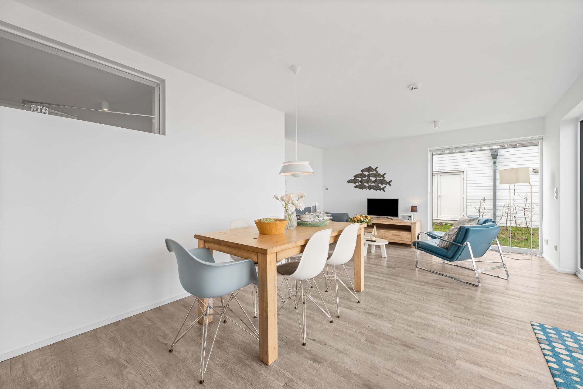 Helles Wohnzimmer mit Esstisch, Stühlen, Sessel, Fernseher und großem Fenster zum Garten.