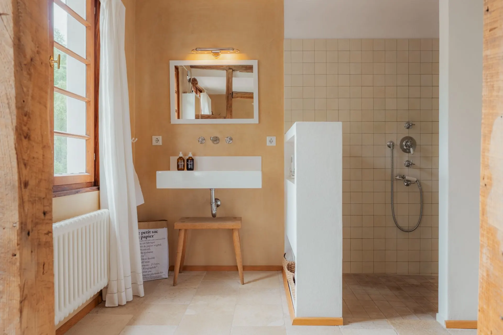 Modernes Badezimmer mit Waschbecken, Spiegel, Holzbank und ebenerdiger Dusche.