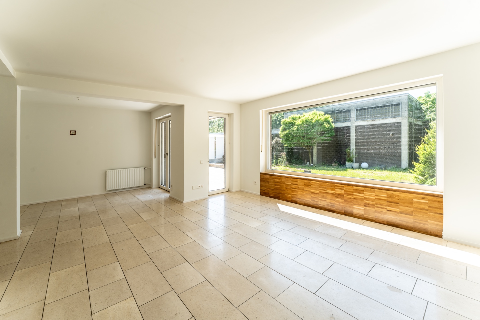 Heller, leerer Raum mit Fliesenboden und großem Fenster mit Blick auf Garten.