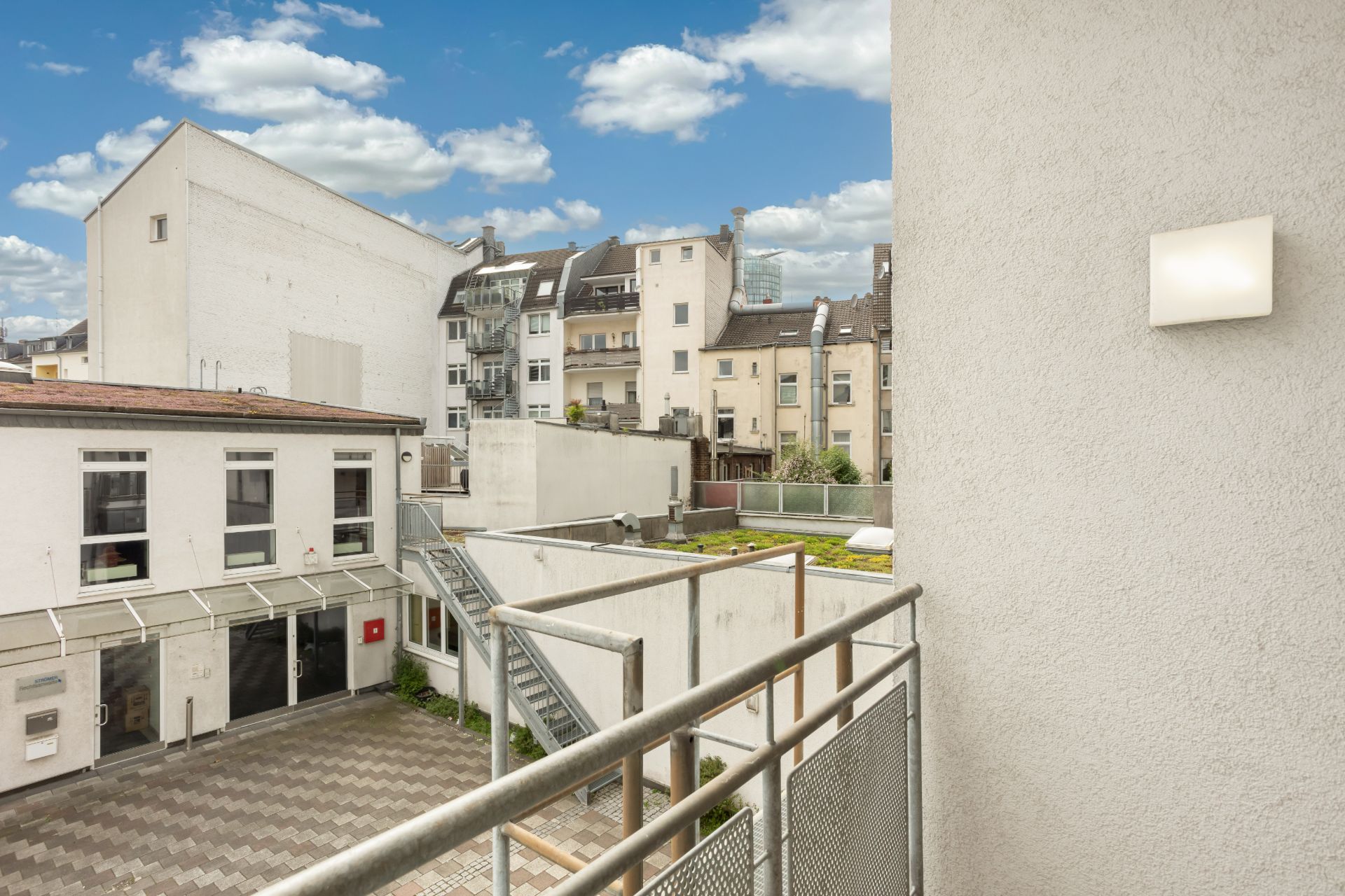 Blick von einem Balkon auf einen Innenhof mit umliegenden Wohnhäusern bei Tageslicht.