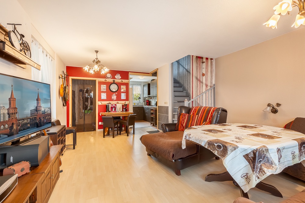 Wohnzimmer mit Fernseher, Esstisch, Couch, dekorierter Wand und offener Blick zur Küche.