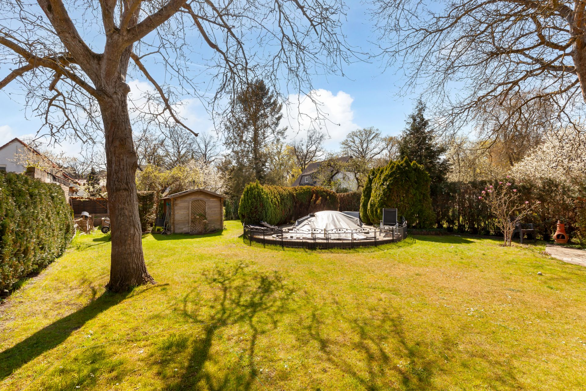 Garten mit grünem Rasen, Bäumen, einer Hütte und einem abgedeckten Pool in der Mitte.