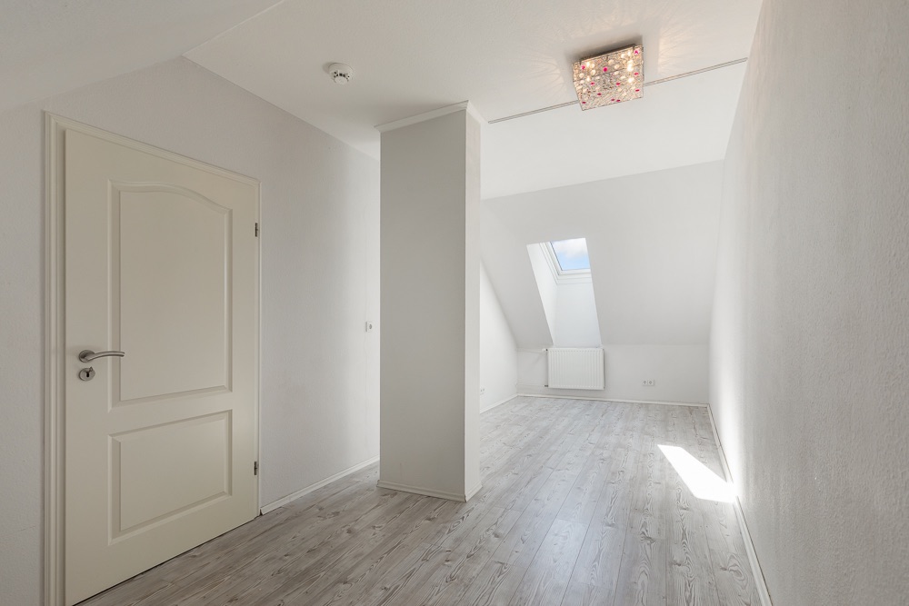 Heller Raum mit weißer Tür, hellen Wänden, Dachfenster und modernem Boden.