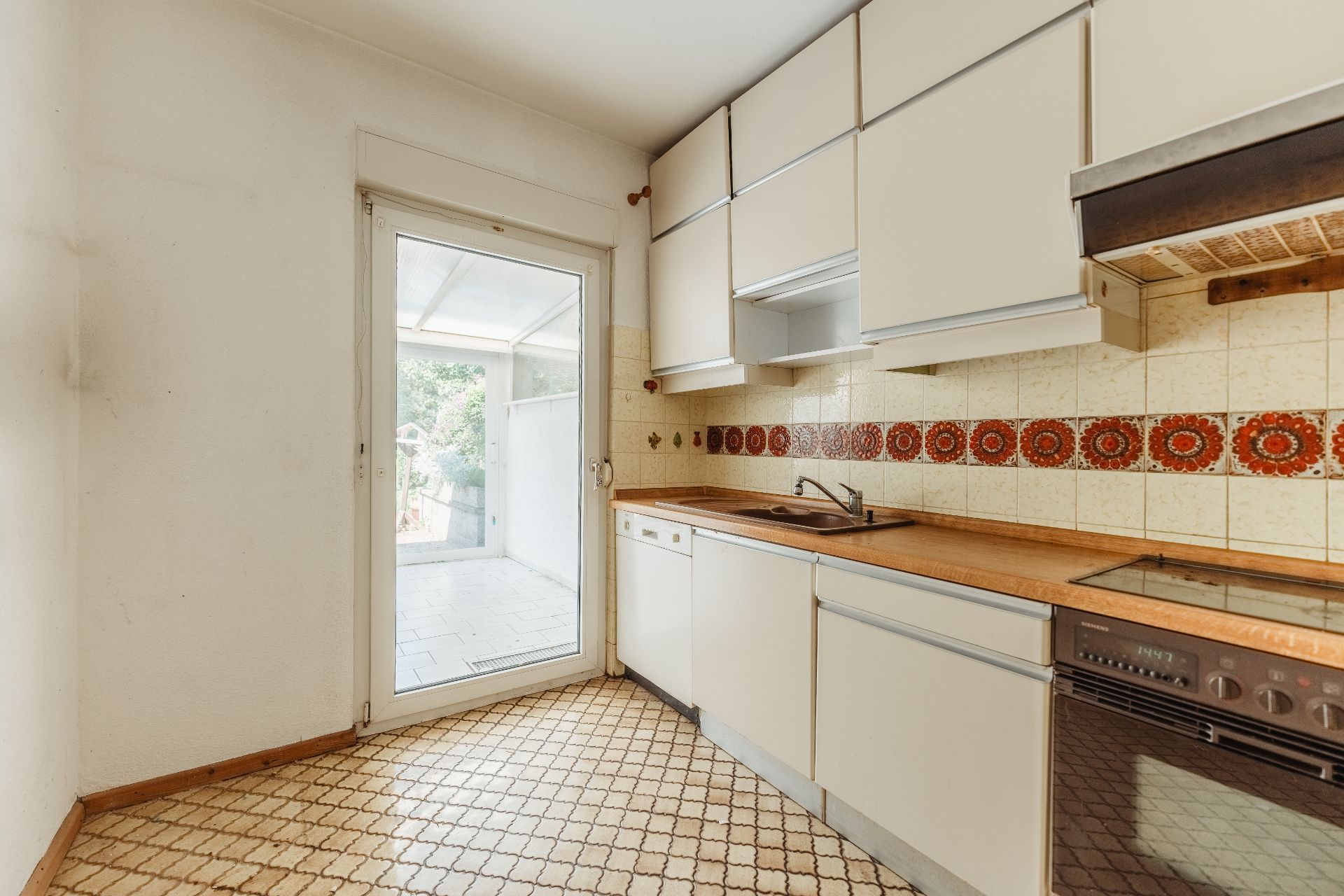 Helle Küche mit weißen Schränken, gemusterter Fliesenwand und Zugang zur Terrasse.