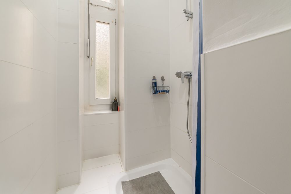 Helle, schmale Dusche mit Fenster, Duschkopf und Ablage für Shampoo an der Wand.