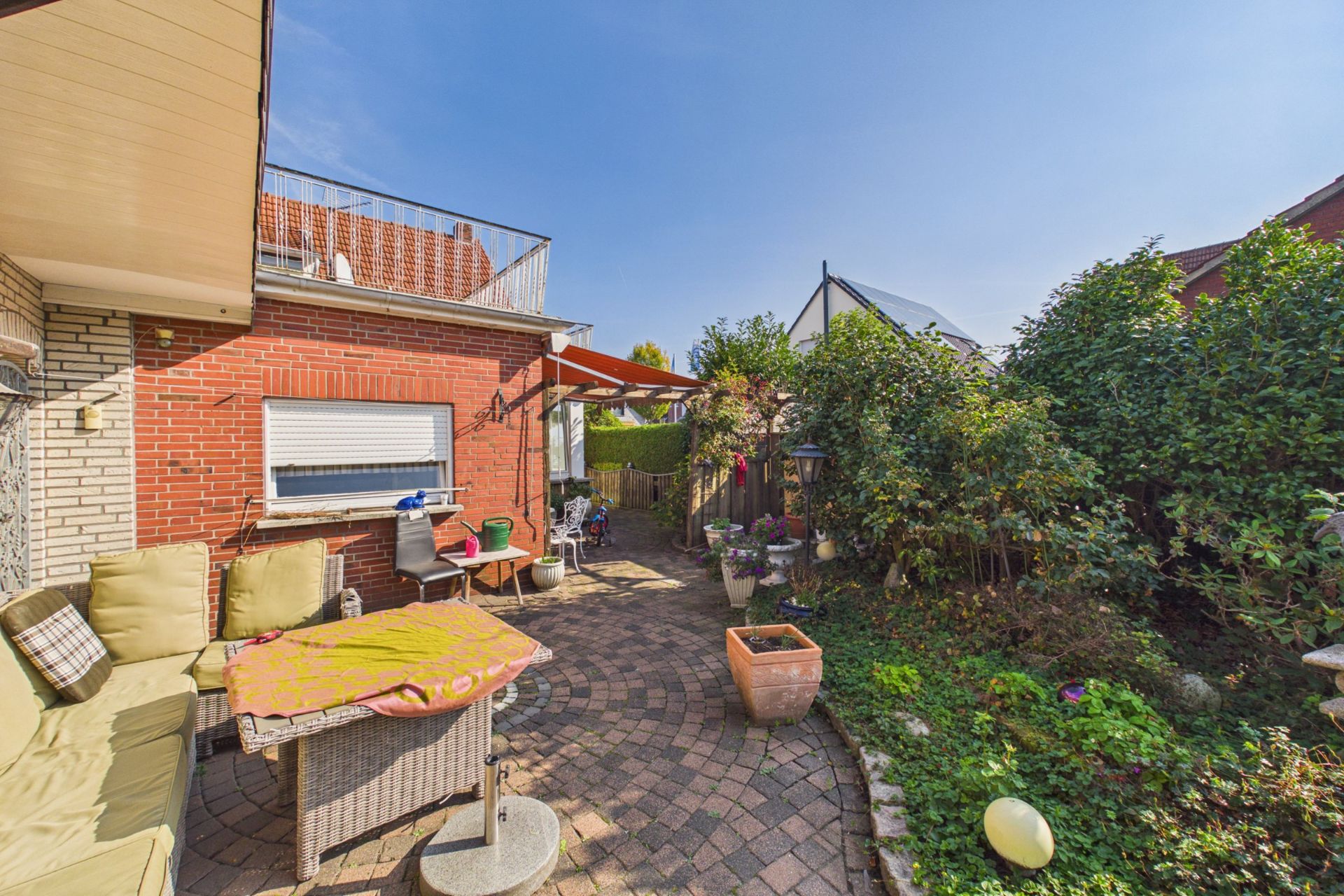 Gepflasterte Terrasse mit Sitzmöbeln, Blumentöpfen und Blick auf einen kleinen Garten.