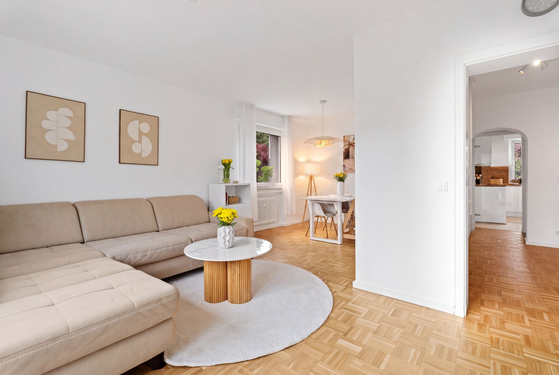 Helles Wohnzimmer mit beiger Eckcouch, rundem Tisch, Esstisch und Blick in die Küche.