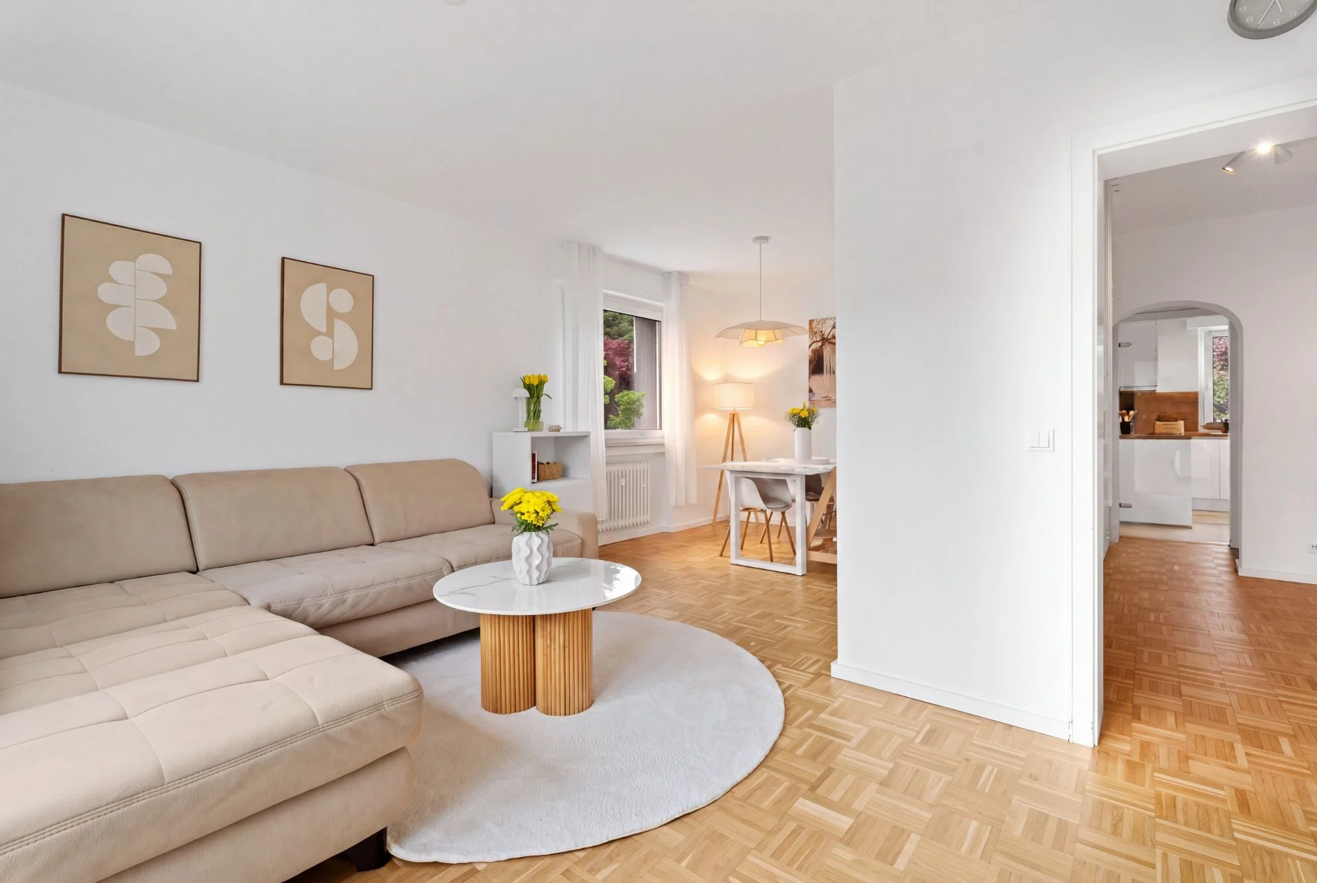 Helles Wohnzimmer mit beiger Eckcouch, rundem Tisch, Esstisch und Blick in die Küche.