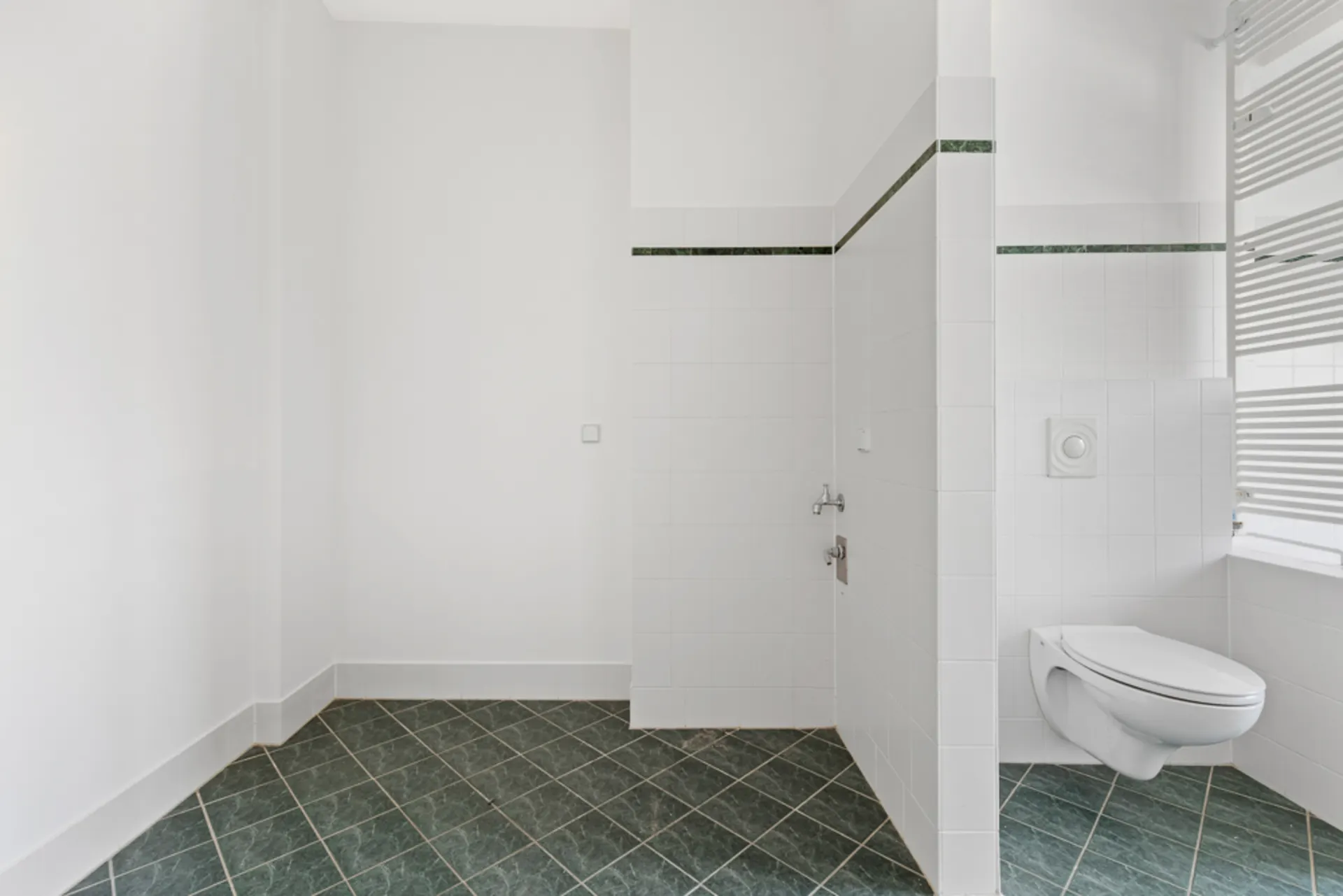 Helles Badezimmer mit grünen Fliesen und Wand-WC, rechteckigem Fenster mit Jalousien.
