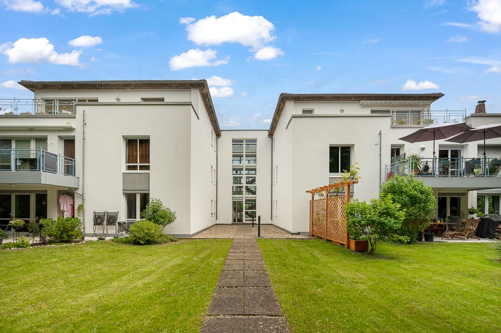 Zwei moderne Wohngebäude mit Balkonen und gepflegtem Garten im Vordergrund.