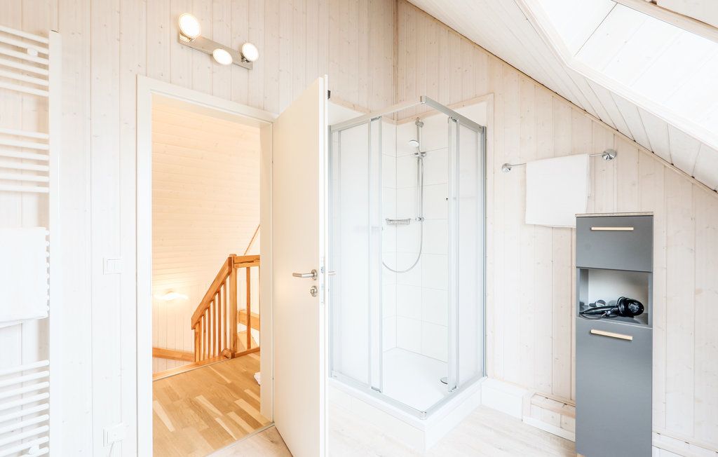 Helles Badezimmer mit Dusche, offenem Regal, Handtuchhalter und Blick auf eine Treppe.