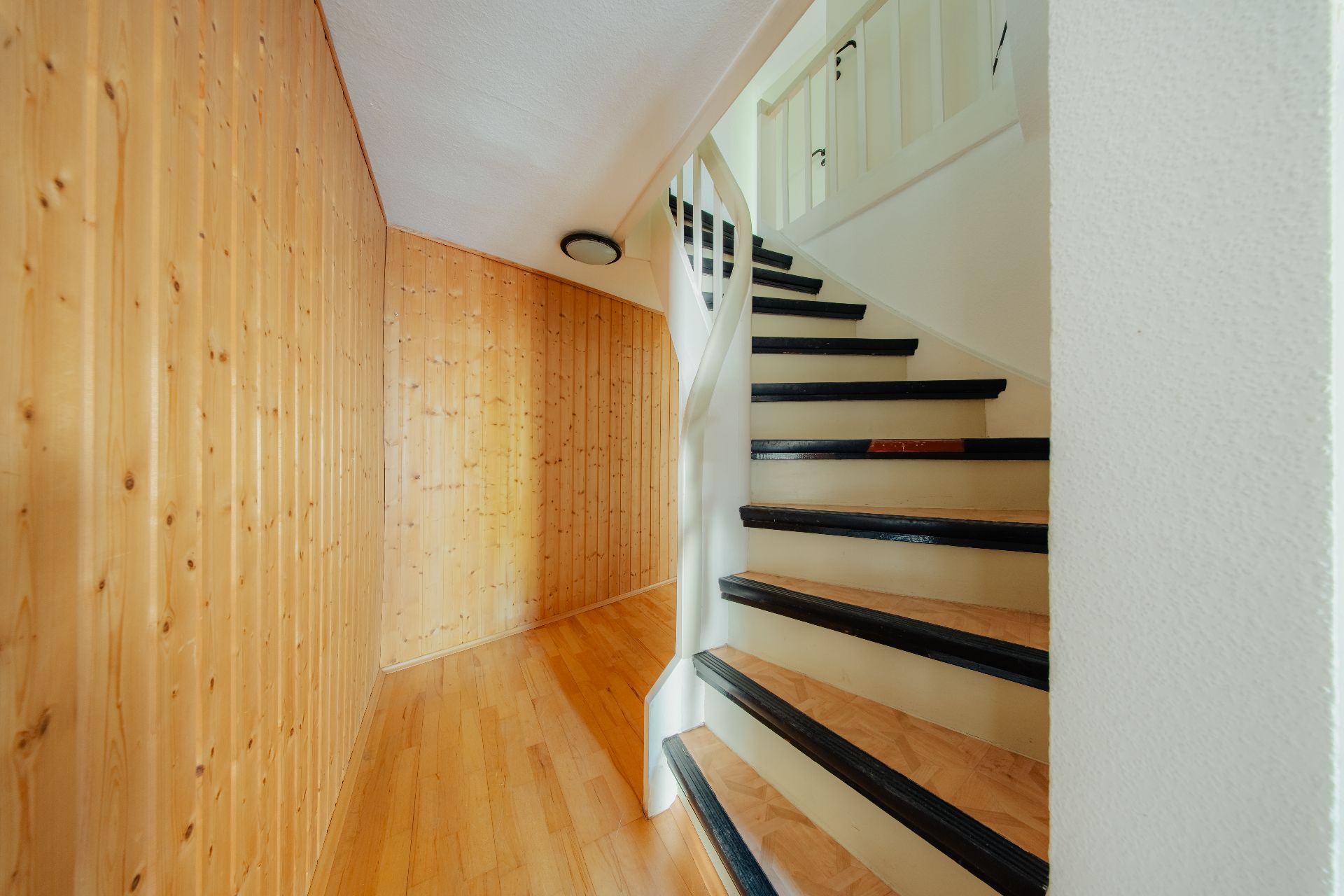 Helles Treppenhaus mit Holzverkleidung an der Wand und einer weißen Holztreppe.