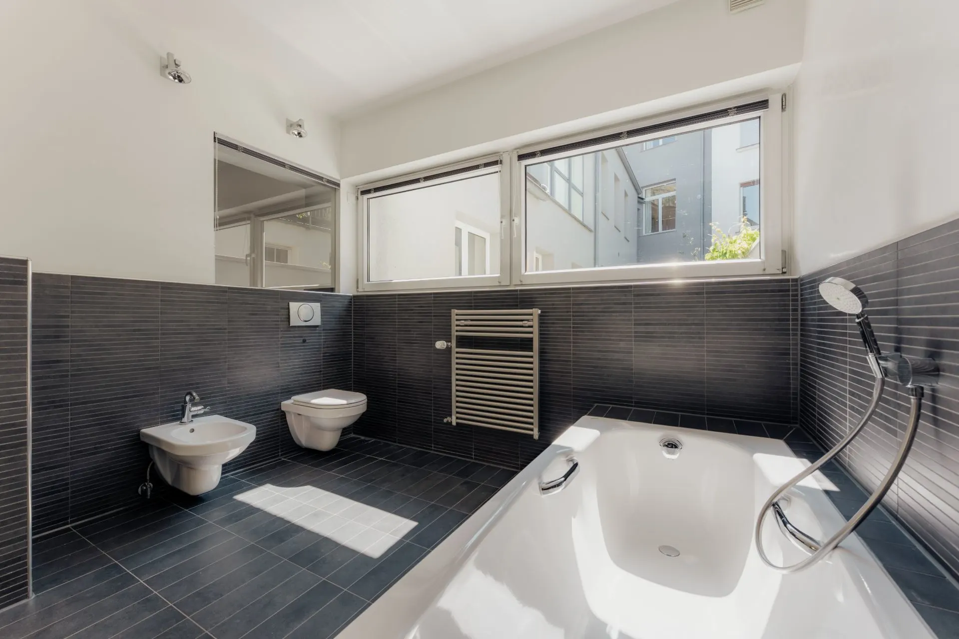 Modernes Badezimmer mit Badewanne, Bidet, WC, Handtuchheizkörper und großem Fenster.