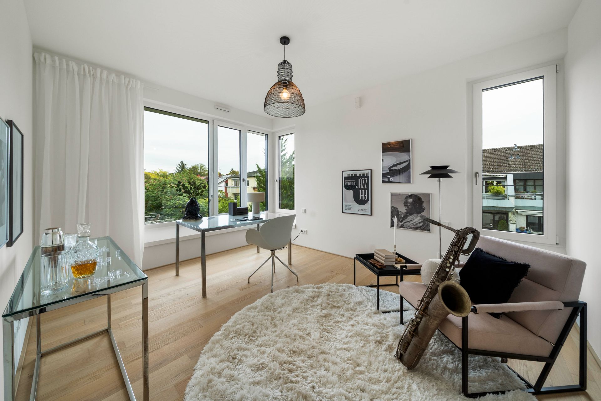 Helles Arbeitszimmer mit Schreibtisch, Sessel, Saxophon und großen Fenstern, Holzboden, weißer Teppich.