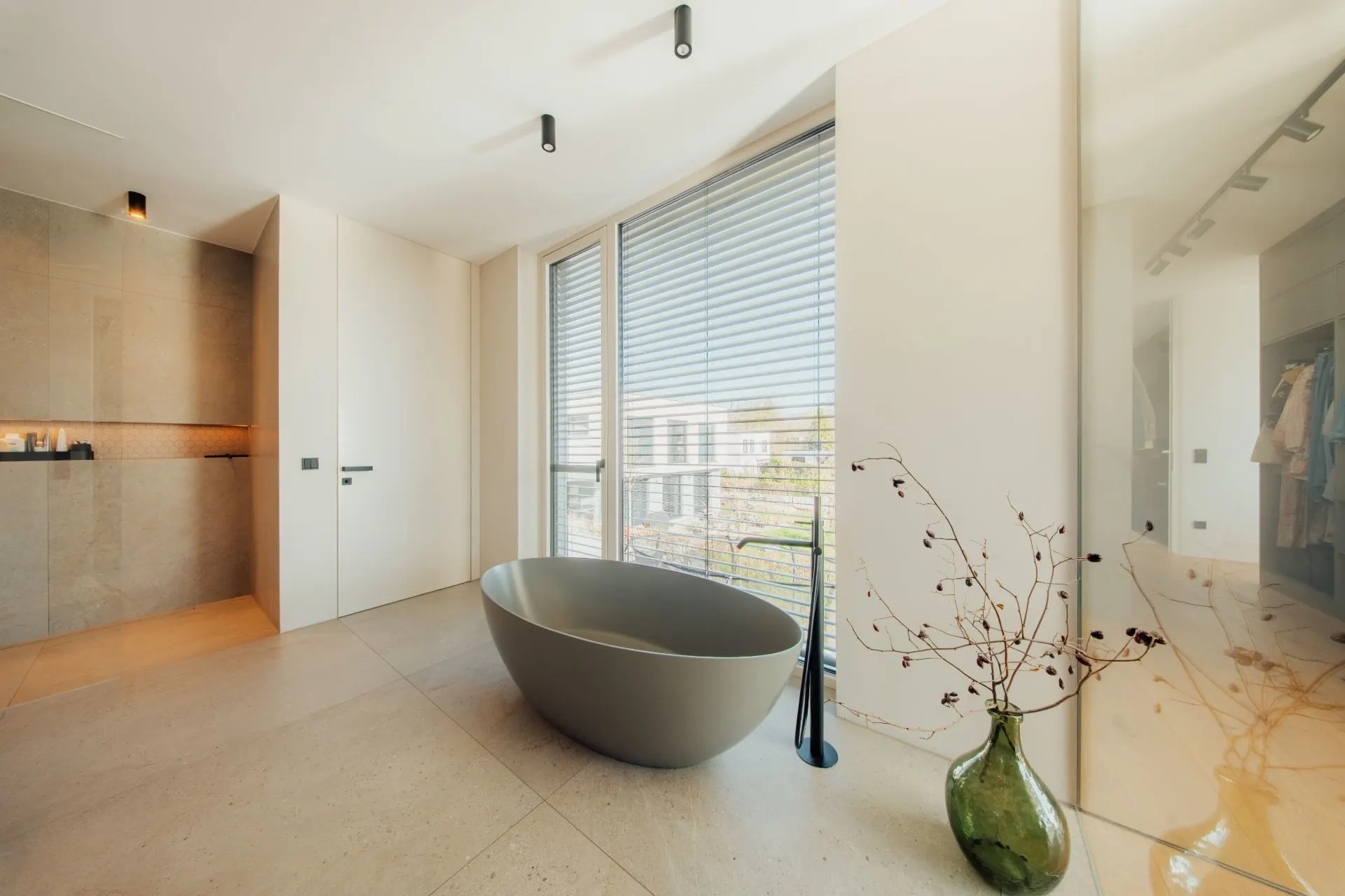 Modernes Badezimmer mit freistehender Badewanne, großen Fenstern und einer Vase mit Zweigen.