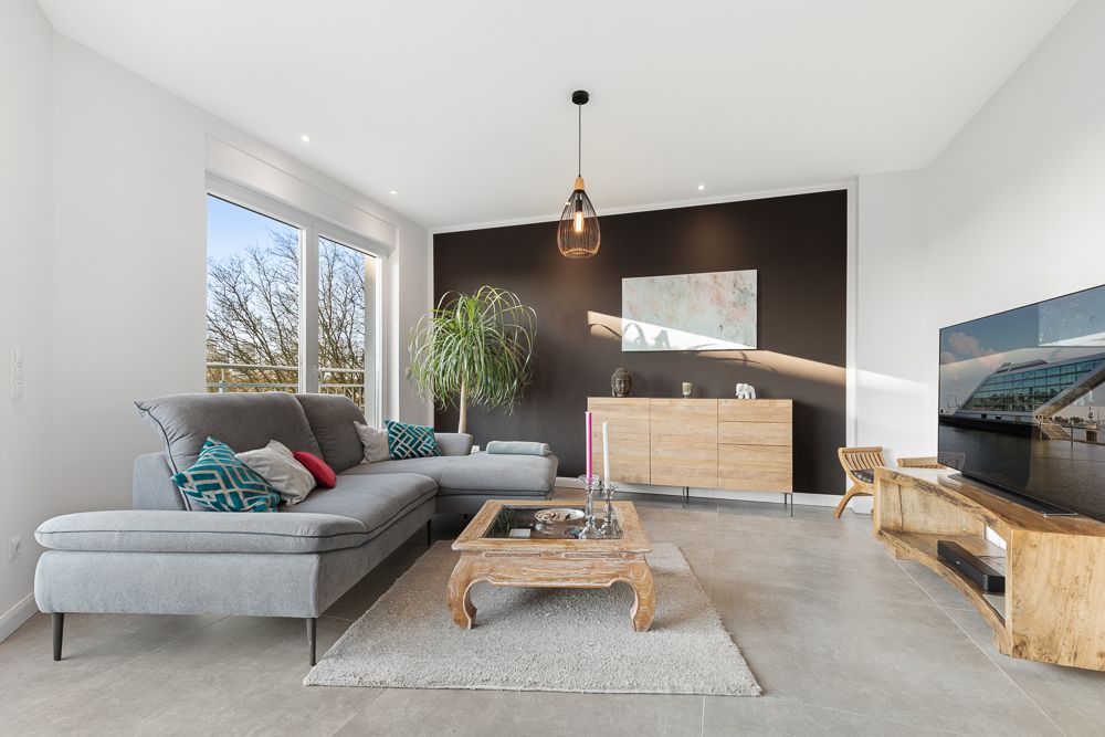 Modernes Wohnzimmer mit grauem Sofa, Holztisch, Sideboard, Fernseher und großer Fensterfront.