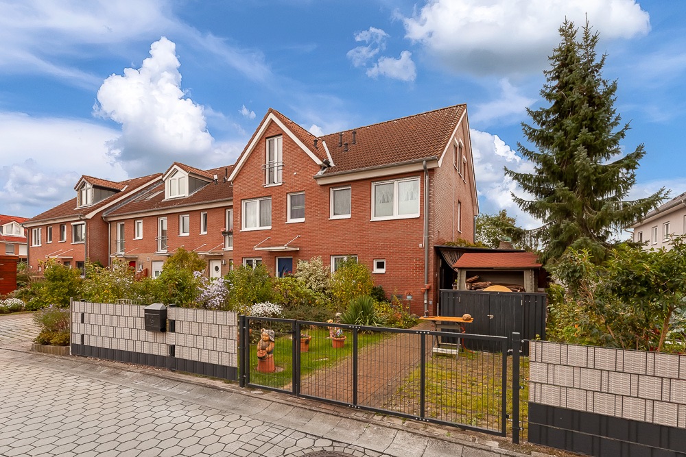 Reihenhaus aus rotem Backstein mit Garten, Zaun und großer Tanne im Vordergrund.