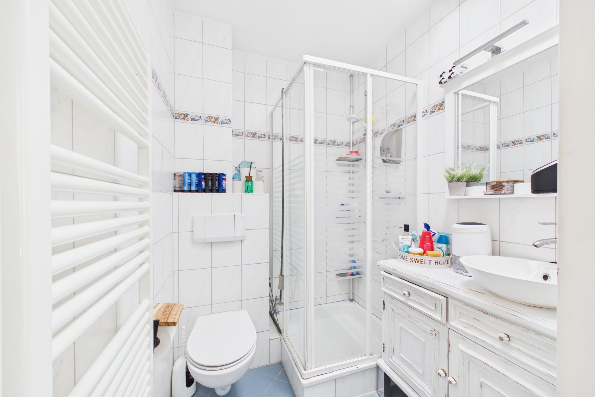 Helles Badezimmer mit Dusche, WC, Waschbecken und Spiegel, weiße Fliesen an Wand und Boden.