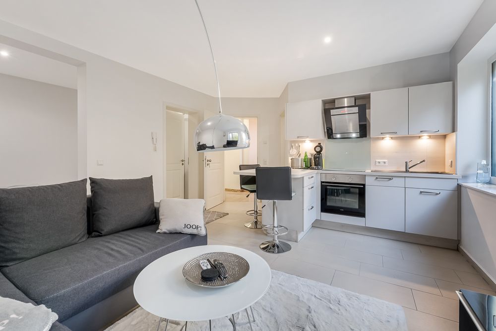 Moderne Wohnküche mit grauem Sofa, Essbereich und Einbauküche mit Elektrogeräten.