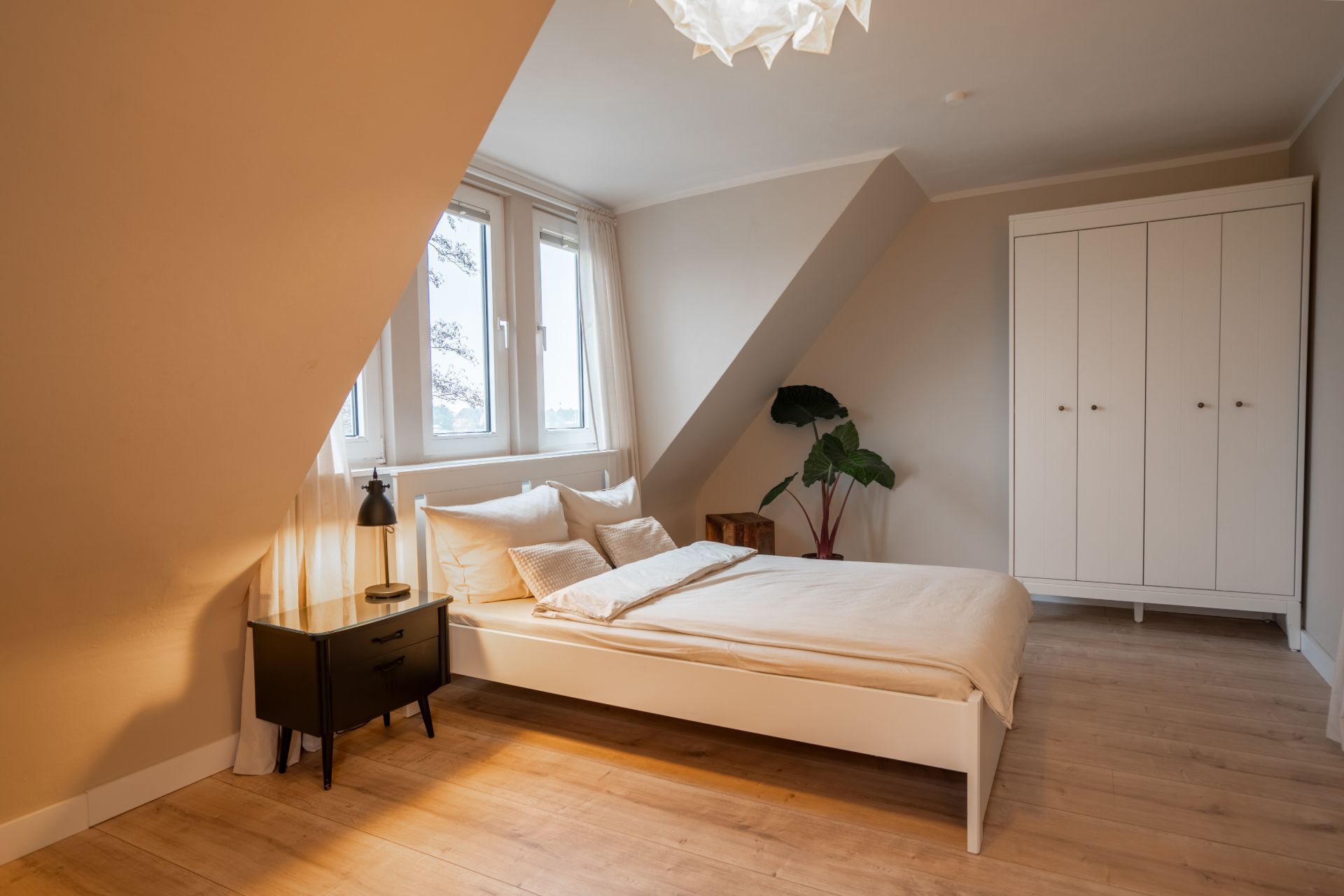 Helles Schlafzimmer mit Bett, Nachttisch, Kleiderschrank und schrägen Wänden.