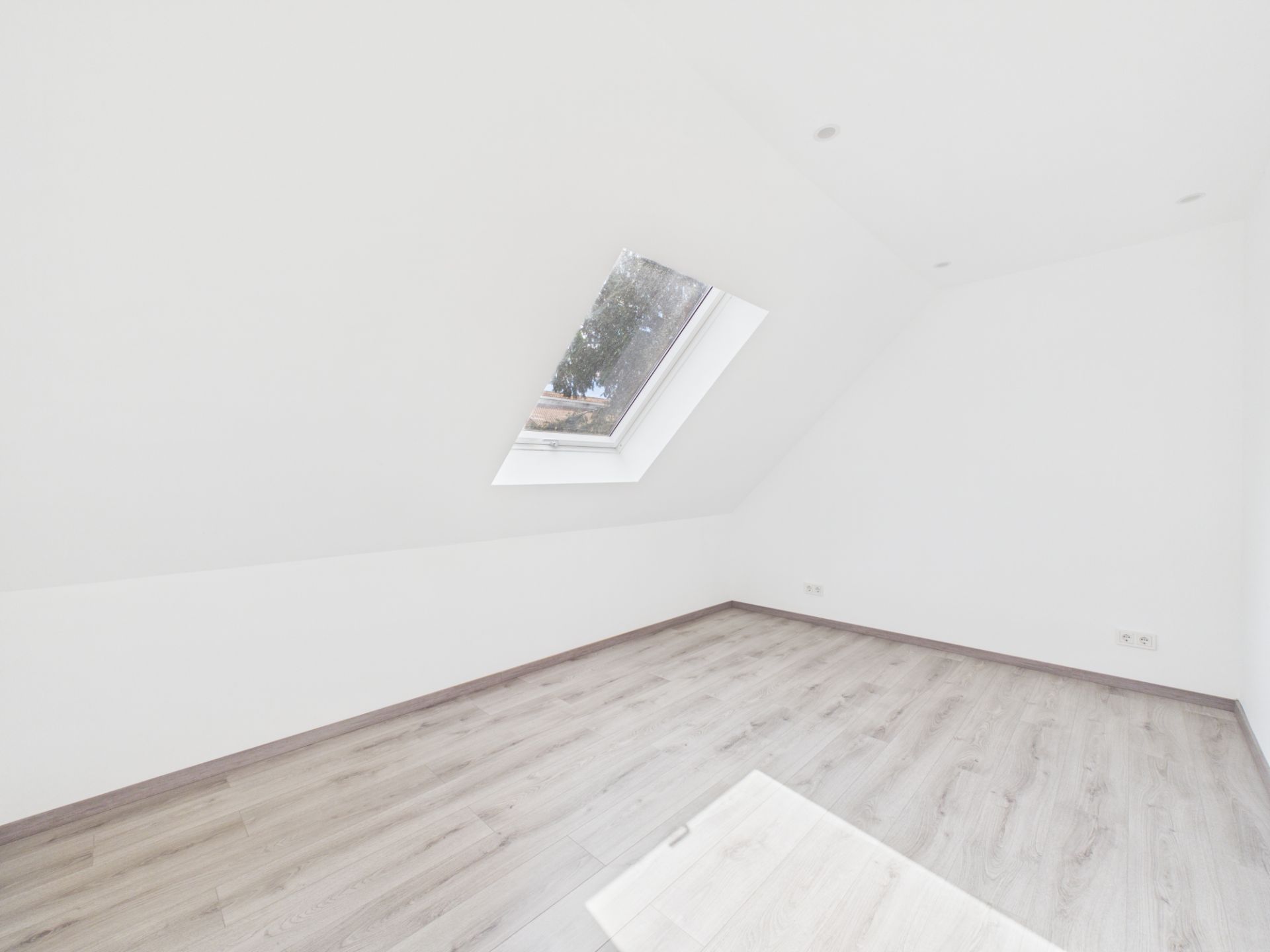 Heller Dachraum mit schräger Decke, großem Dachfenster und hellem Holzboden.