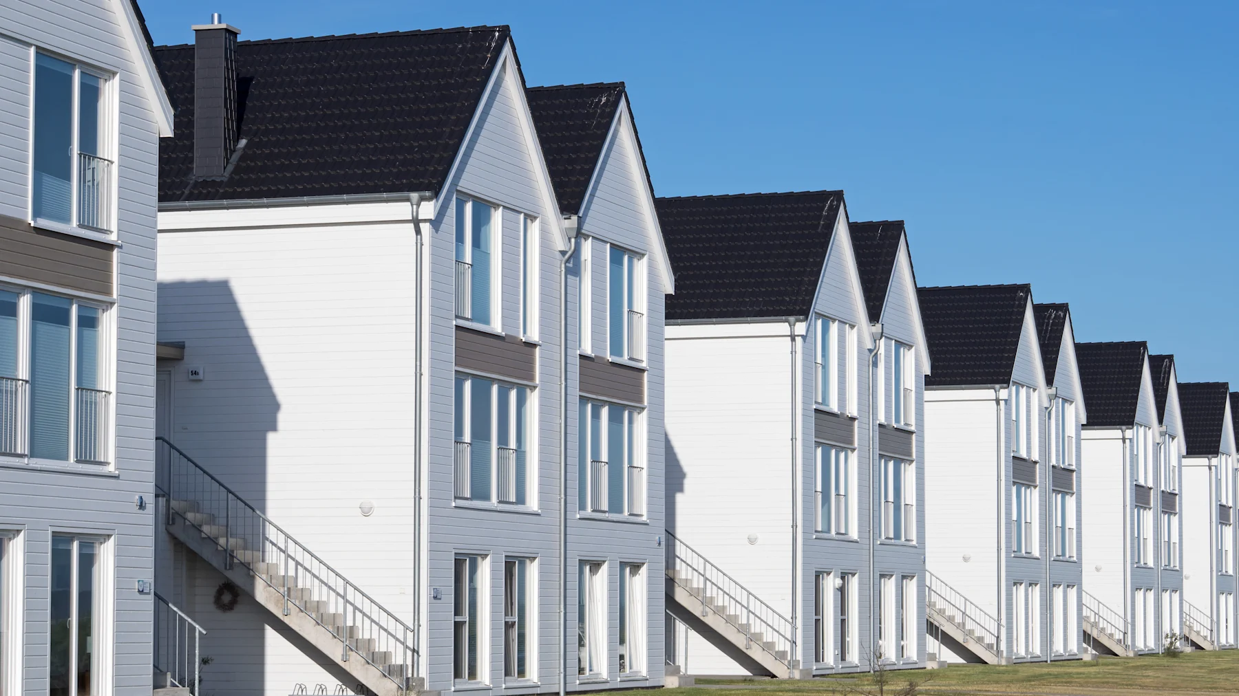 Reihe moderner, weißer Wohnhäuser mit schwarzen Dächern und Außentreppen.