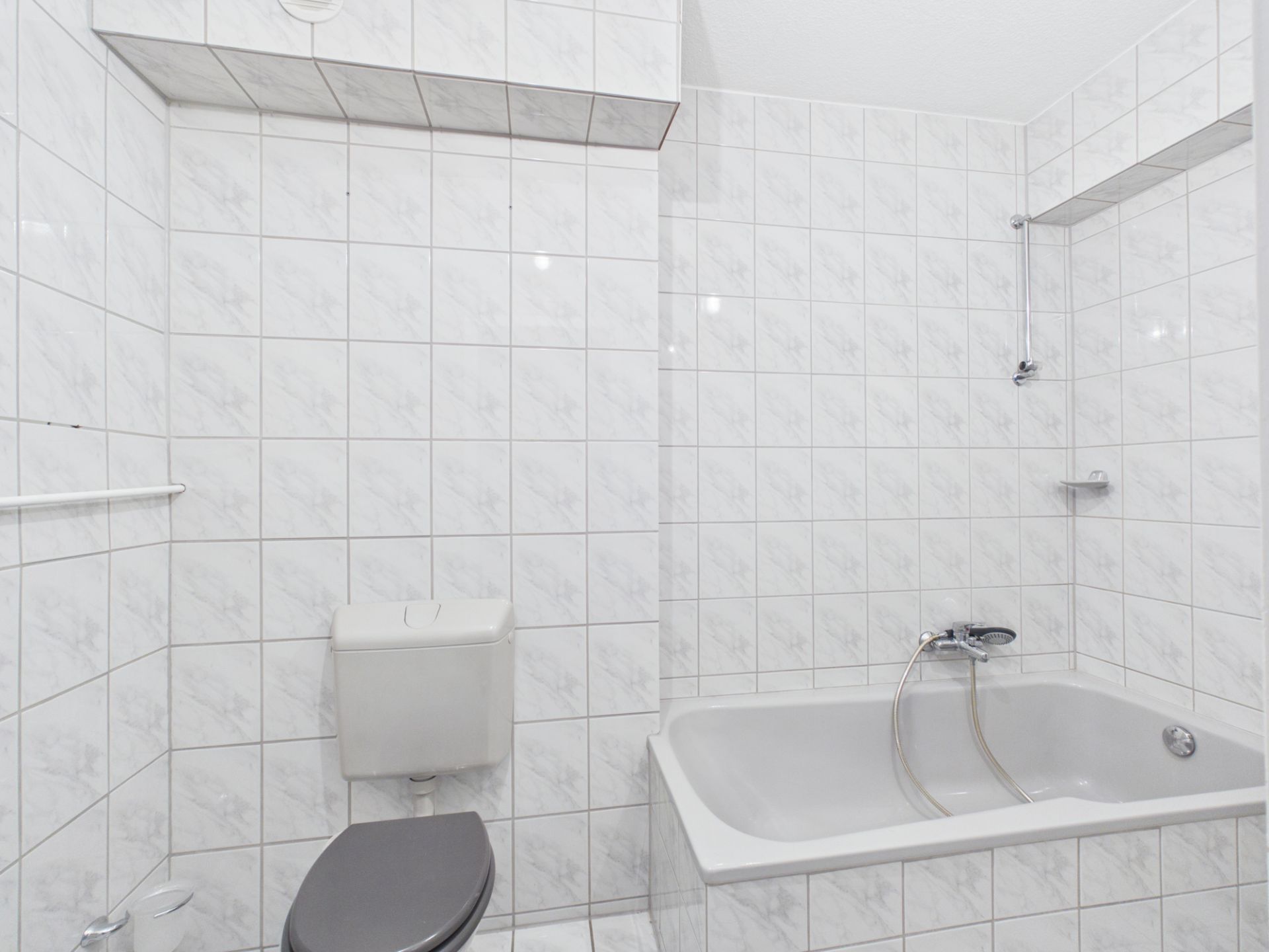 Badezimmer mit Badewanne, Duschbrause und Toilette, komplett gefliest.