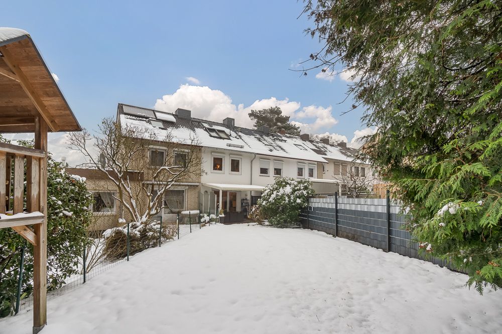 Reihenhaus mit verschneitem Garten, Bäumen und Holzstruktur im Vordergrund.
