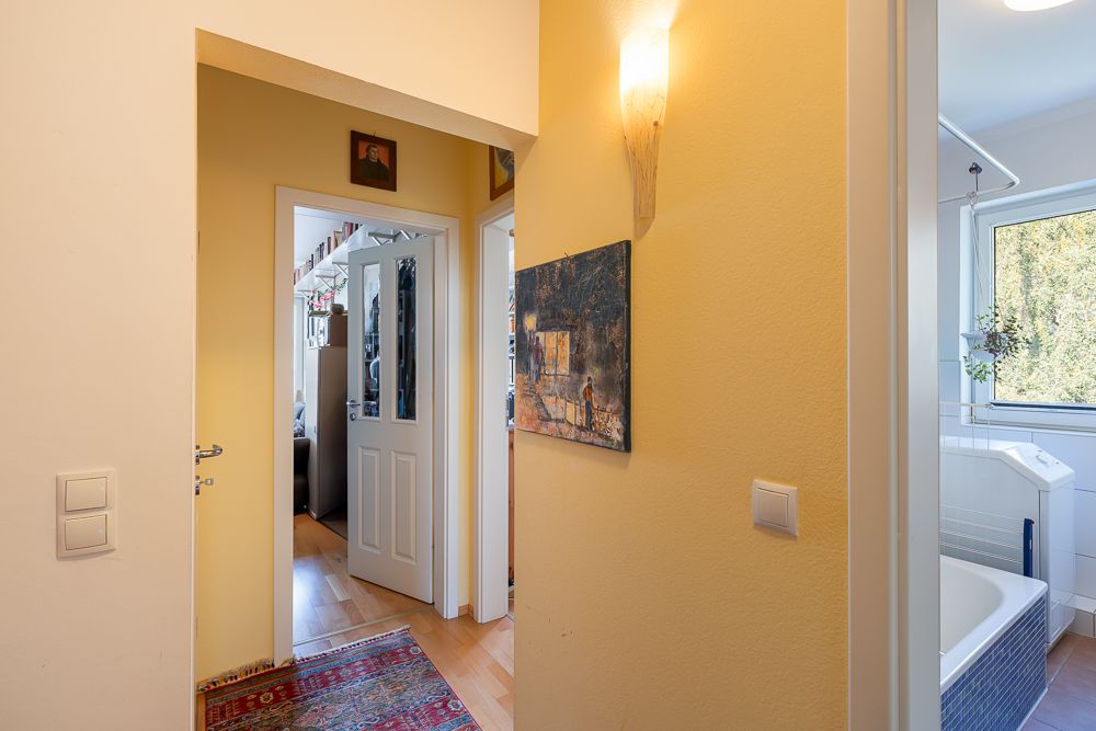 Heller Flur mit Teppich, Wandlampe und Blick ins Badezimmer mit Fenster.