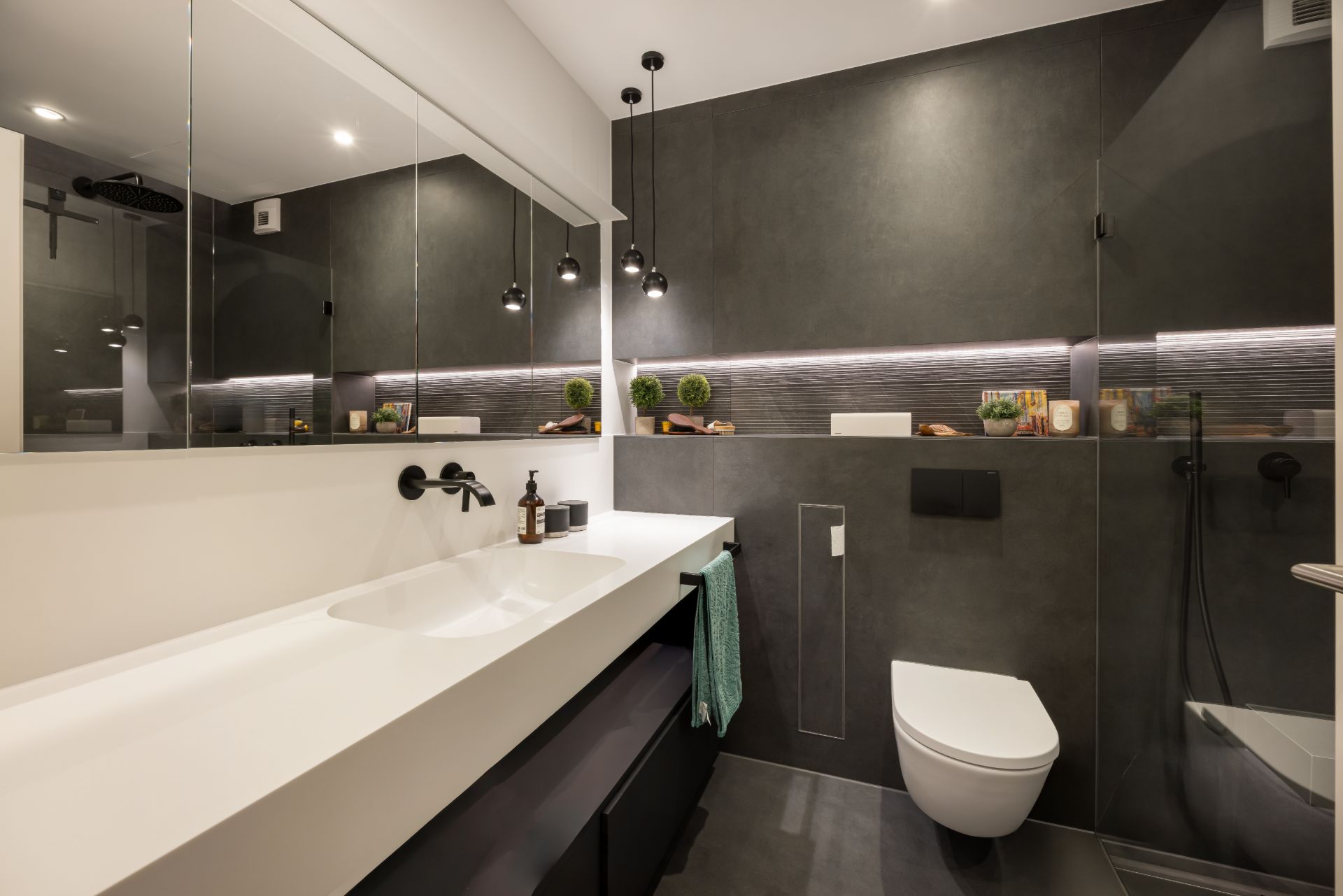 Modernes Badezimmer mit großem Spiegel, Hängelampen, Waschbecken und Wandtoilette.