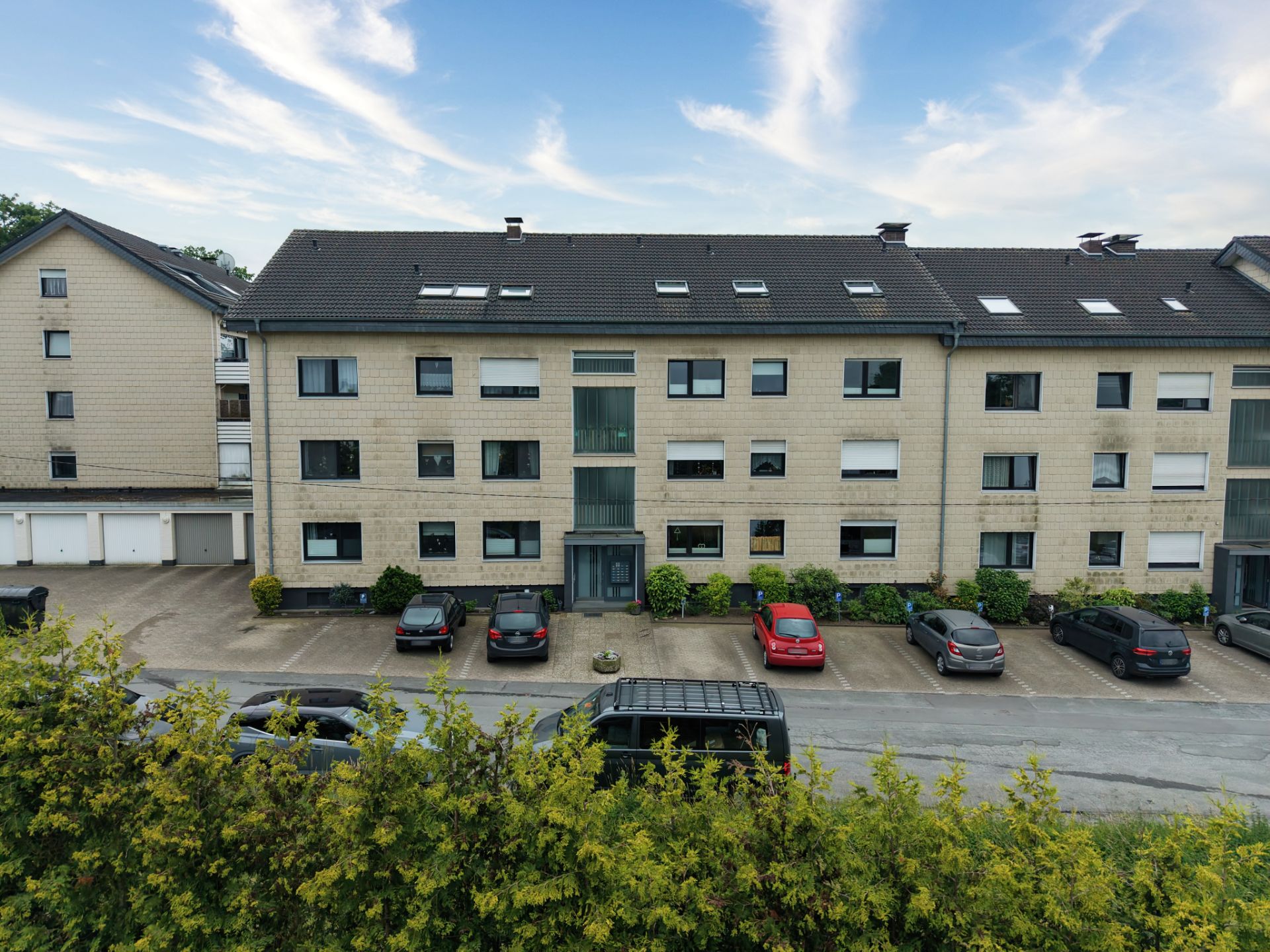 Modernes Wohnhaus mit mehreren Etagen, Garagen und geparkten Autos davor.