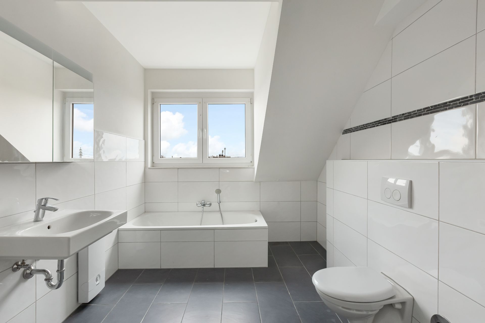 Helles Badezimmer mit Badewanne, Waschbecken und Toilette unter einem Dachfenster.